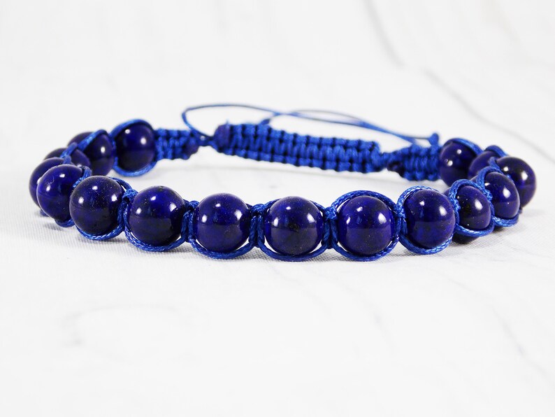 May include: A blue beaded bracelet with a knotted cord. The beads are round and dark blue, and the cord is a lighter shade of blue.