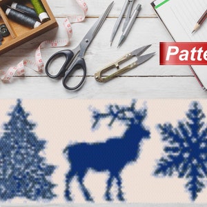 May include: A blue and white cross stitch pattern featuring a Christmas tree, reindeer, and snowflake. The pattern is on a white background and is surrounded by sewing supplies, including scissors, thread, and a measuring tape.