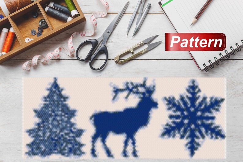 May include: A blue and white cross stitch pattern featuring a Christmas tree, reindeer, and snowflake. The pattern is on a white background and is surrounded by sewing supplies, including scissors, thread, and a measuring tape.