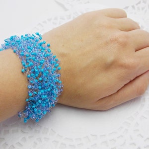 May include: A turquoise and light blue beaded bracelet with a crocheted design. The bracelet is on a white surface.