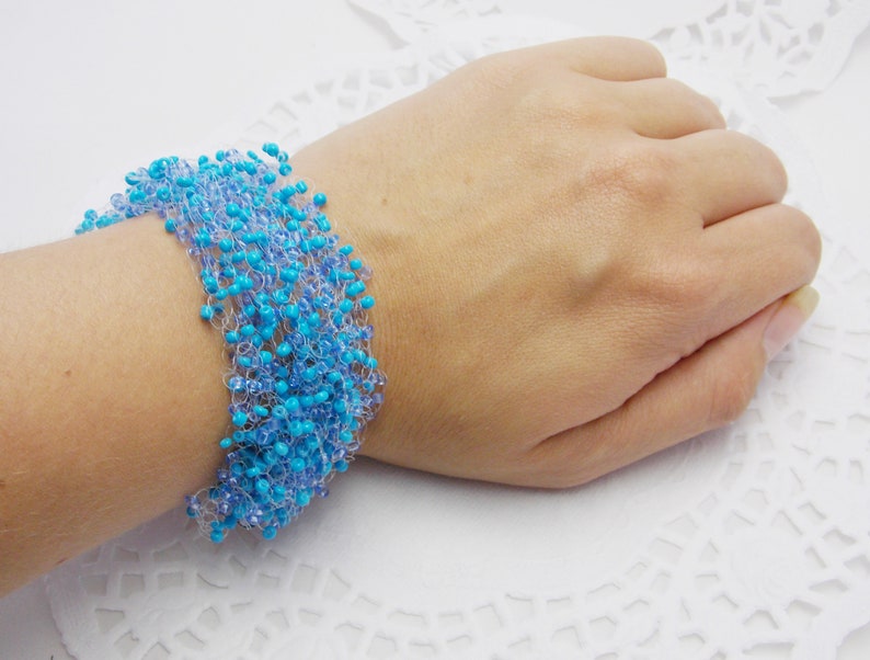May include: A turquoise and light blue beaded bracelet with a crocheted design. The bracelet is on a white surface.
