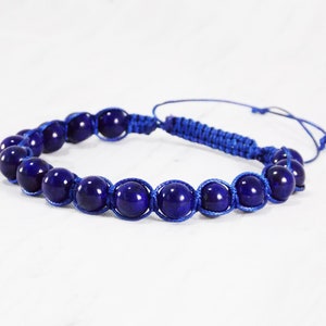 May include: A blue beaded bracelet with a knotted cord. The beads are round and have a dark blue color.