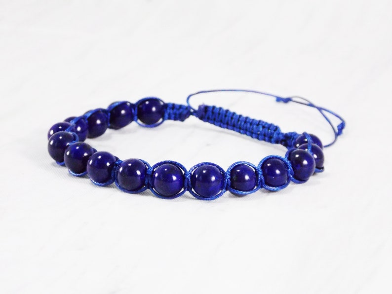 May include: A blue beaded bracelet with a knotted cord. The beads are round and have a dark blue color.