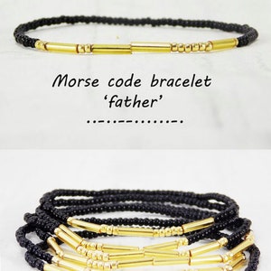 May include: A black beaded bracelet with gold bar beads spelling out the word 'father' in Morse code. The bracelet is shown layered on a white surface.