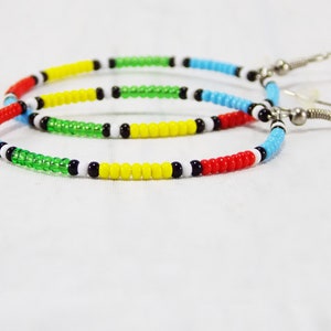May include: A pair of hoop earrings made with colorful beads. The beads are red, yellow, green, blue, white, and black. The earrings are attached to silver hooks.