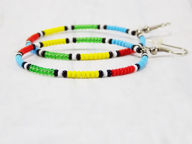 May include: A pair of hoop earrings made with colorful beads. The beads are red, yellow, green, blue, white, and black. The earrings are attached to silver hooks.