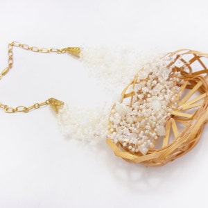 May include: A white beaded necklace with a woven basket design. The necklace is made of small white beads and has a gold chain.