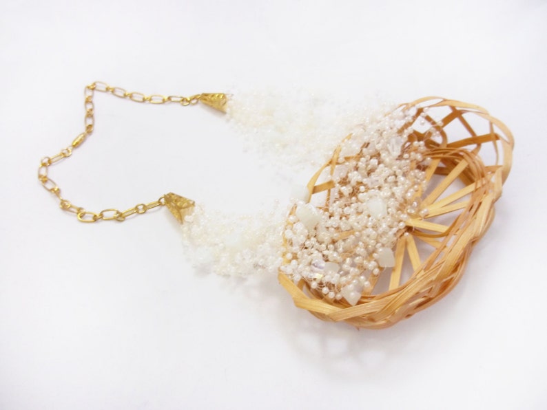 May include: A white beaded necklace with a woven basket design. The necklace is made of small white beads and has a gold chain.