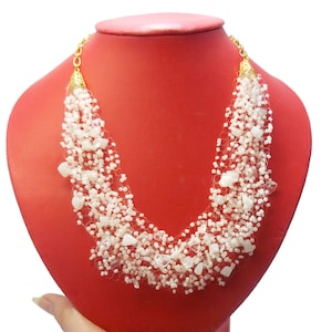 May include: A white beaded necklace with a gold clasp. The necklace is made of small white beads and has a delicate, layered design.