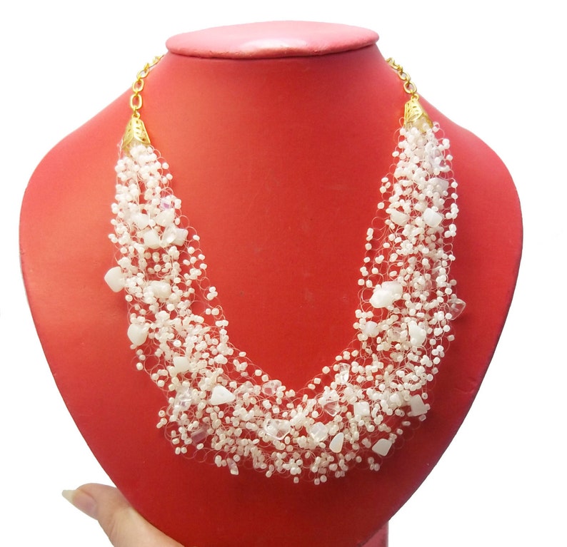 May include: A white beaded necklace with a gold clasp. The necklace is made of small white beads and has a delicate, layered design.
