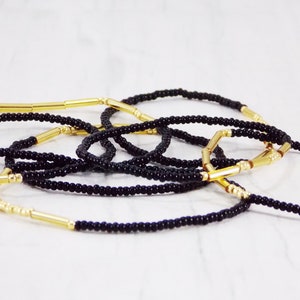 May include: A set of black beaded bracelets with gold spacers. The bracelets are layered and intertwined, creating a visually appealing design.