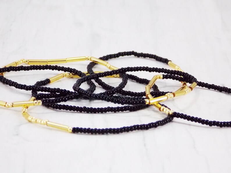 May include: A set of black beaded bracelets with gold spacers. The bracelets are layered and intertwined, creating a visually appealing design.