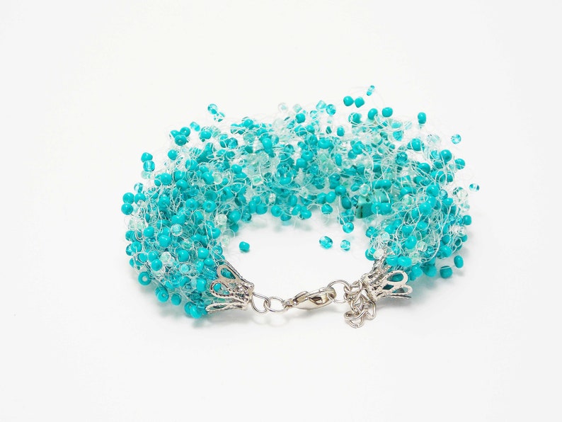 May include: A turquoise and white beaded bracelet with a silver clasp. The beads are clustered together to create a fluffy, cloud-like effect.