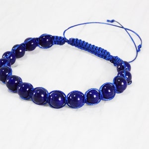 May include: A blue beaded bracelet with a knotted cord closure. The beads are dark blue and round.