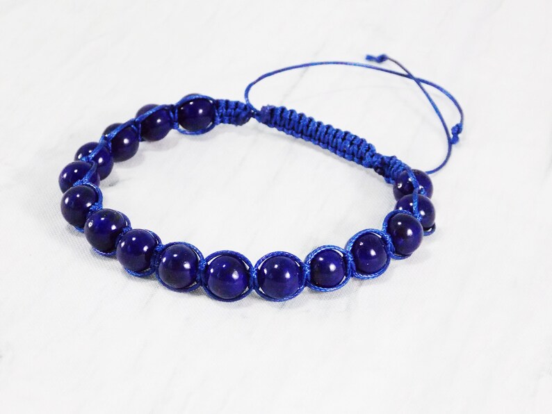 May include: A blue beaded bracelet with a knotted cord closure. The beads are dark blue and round.