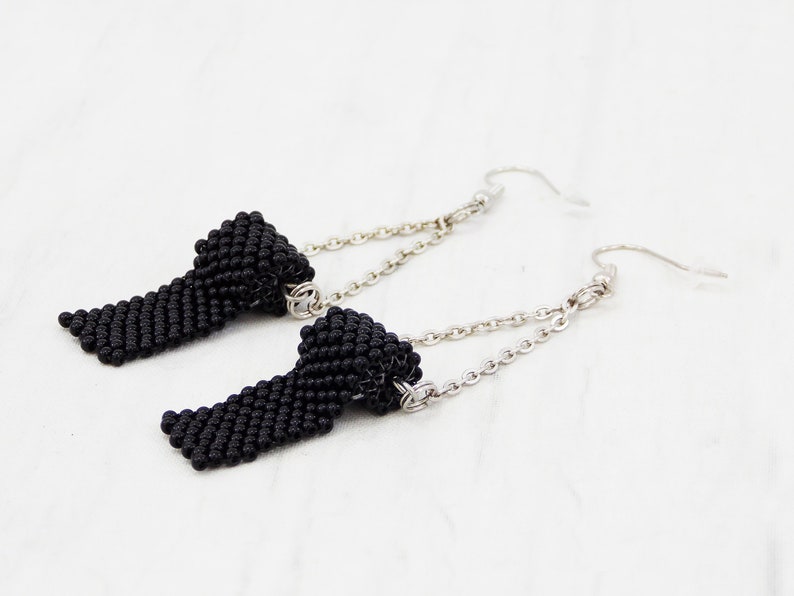 May include: A pair of black beaded earrings with silver chains and hooks. The beads are small and tightly woven, creating a textured look.