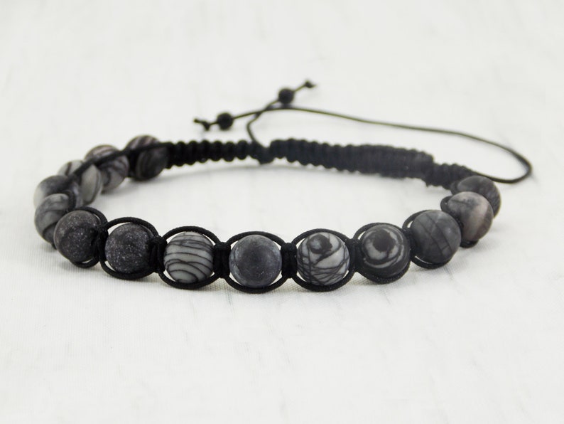 Puede incluir: Pulsera de cord&oacute;n negro con cuentas de piedra con patrones en blanco y negro. La pulsera tiene un cierre de nudo deslizante.