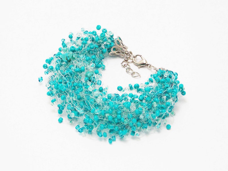 May include: A turquoise beaded bracelet with a silver clasp. The beads are strung on a thin, clear thread, creating a delicate and airy look.