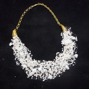 May include: A white beaded necklace with a gold chain and clasp. The beads are small and clustered together, creating a cascading effect.