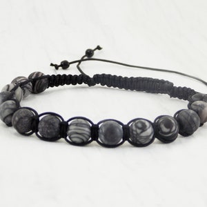 Puede incluir: Un brazalete negro con cuentas de cord&oacute;n negro y cuentas con patrones plateados y negros.