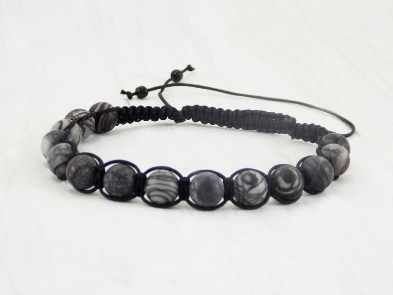 Puede incluir: Un brazalete negro con cuentas de cord&oacute;n negro y cuentas con patrones plateados y negros.