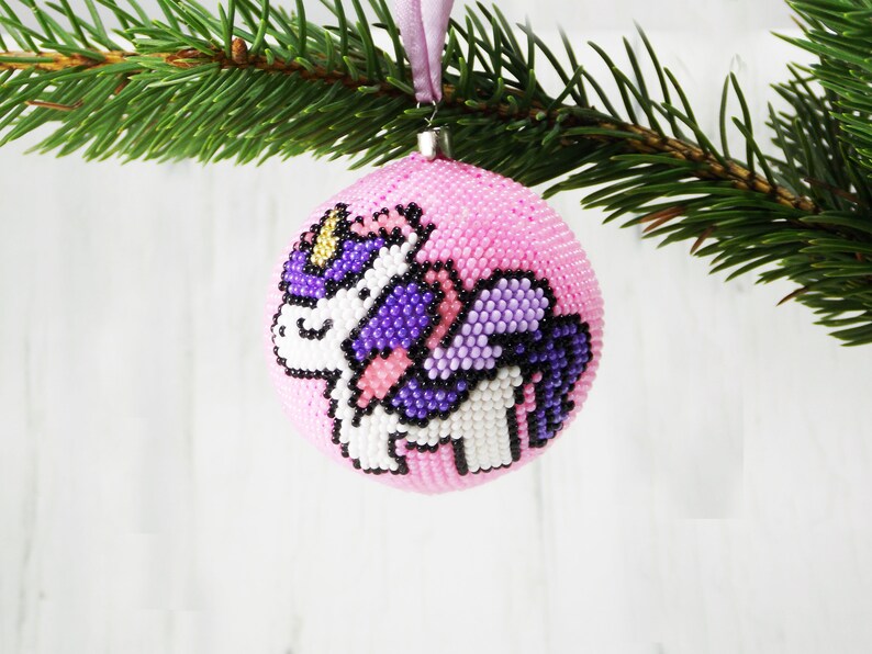 May include: Pink Christmas ornament with a beaded unicorn design. The unicorn is purple, white, and black.