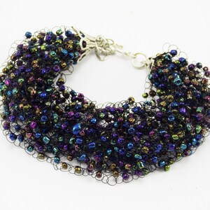 May include: A black beaded bracelet with iridescent beads in shades of blue, green, and purple. The beads are woven into a delicate net-like pattern.