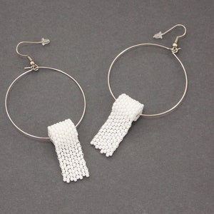May include: A pair of silver hoop earrings with white beaded toilet paper roll charms hanging from them.