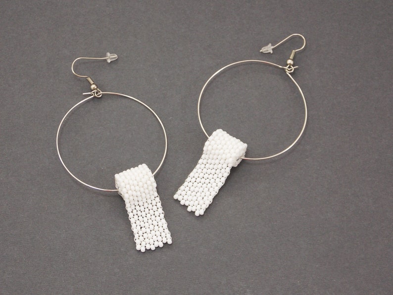 May include: A pair of silver hoop earrings with white beaded toilet paper roll charms hanging from them.