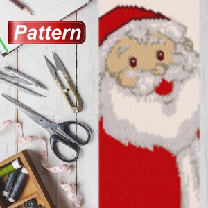 May include: A bead pattern for a Santa Claus ornament. The pattern is made up of red, white, and beige beads. The pattern is for a Santa Claus with a red hat, white beard, and red suit.