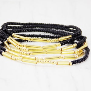 May include: A set of black and gold beaded bracelets. The bracelets are made with small black beads and gold spacer beads. The bracelets are stacked on top of each other.