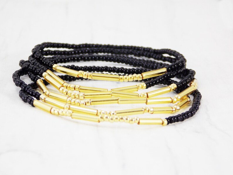 May include: A set of black and gold beaded bracelets. The bracelets are made with small black beads and gold spacer beads. The bracelets are stacked on top of each other.