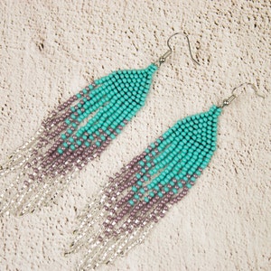 May include: A pair of long, beaded earrings with a gradient of turquoise and purple beads. The earrings have silver accents and silver hooks.