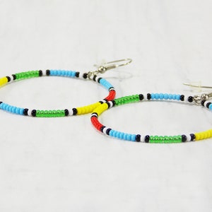 May include: A pair of hoop earrings made with colorful beads. The beads are arranged in a pattern of red, yellow, green, blue, black, and white.