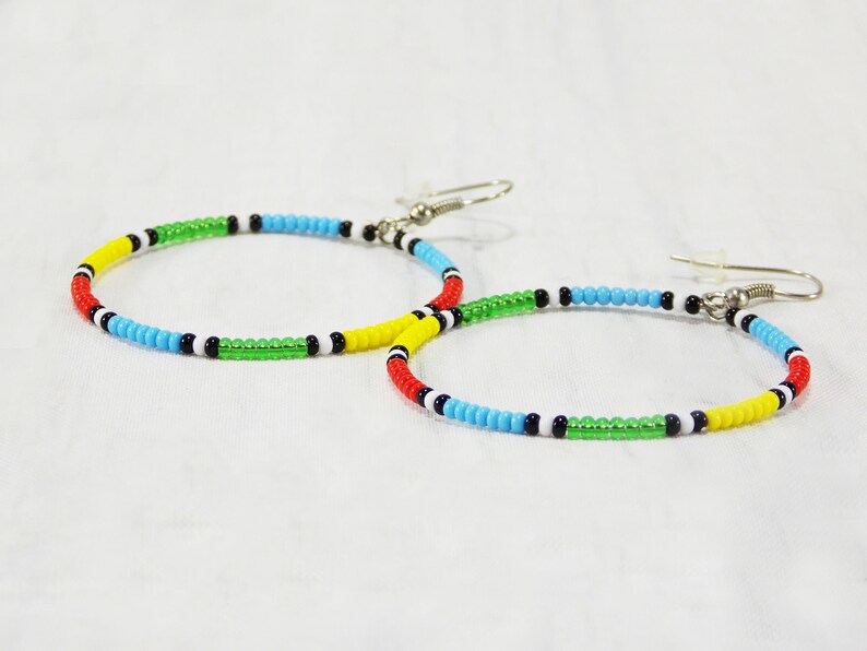 May include: A pair of hoop earrings made with colorful beads. The beads are arranged in a pattern of red, yellow, green, blue, black, and white.