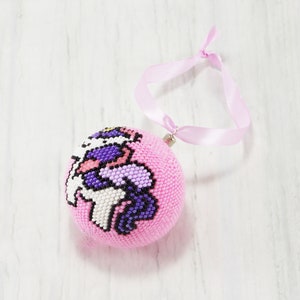 May include: Pink beaded Christmas ornament with a unicorn design. The ornament has a pink ribbon attached for hanging.