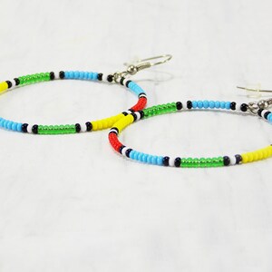 May include: A pair of hoop earrings made with colorful beads. The beads are red, yellow, green, blue, black, and white. The earrings have silver hooks.