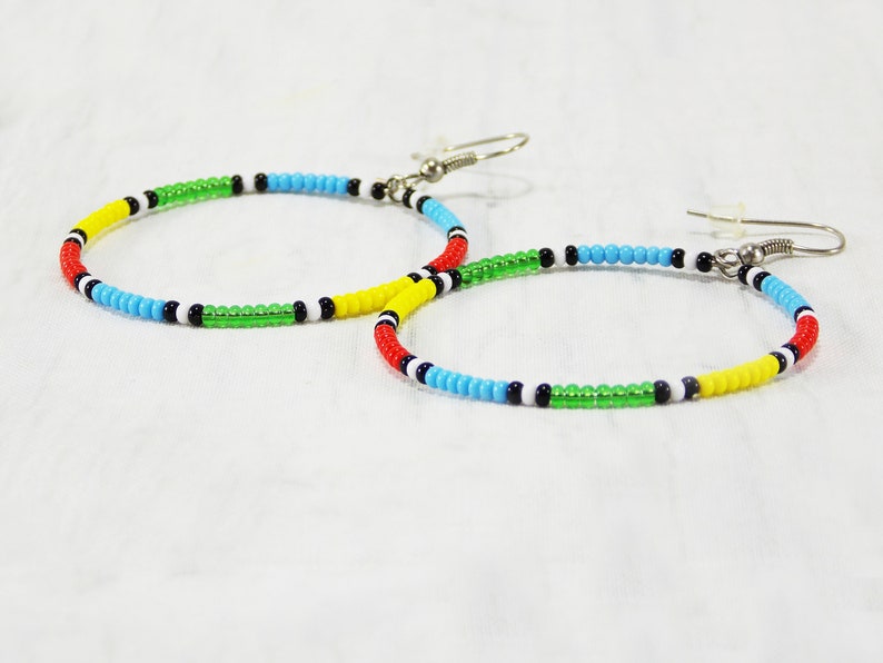 May include: A pair of hoop earrings made with colorful beads. The beads are red, yellow, green, blue, black, and white. The earrings have silver hooks.