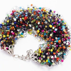May include: A colorful beaded bracelet with a black crocheted design and silver clasps. The beads are a mix of colors, including red, orange, yellow, green, blue, purple, and white.