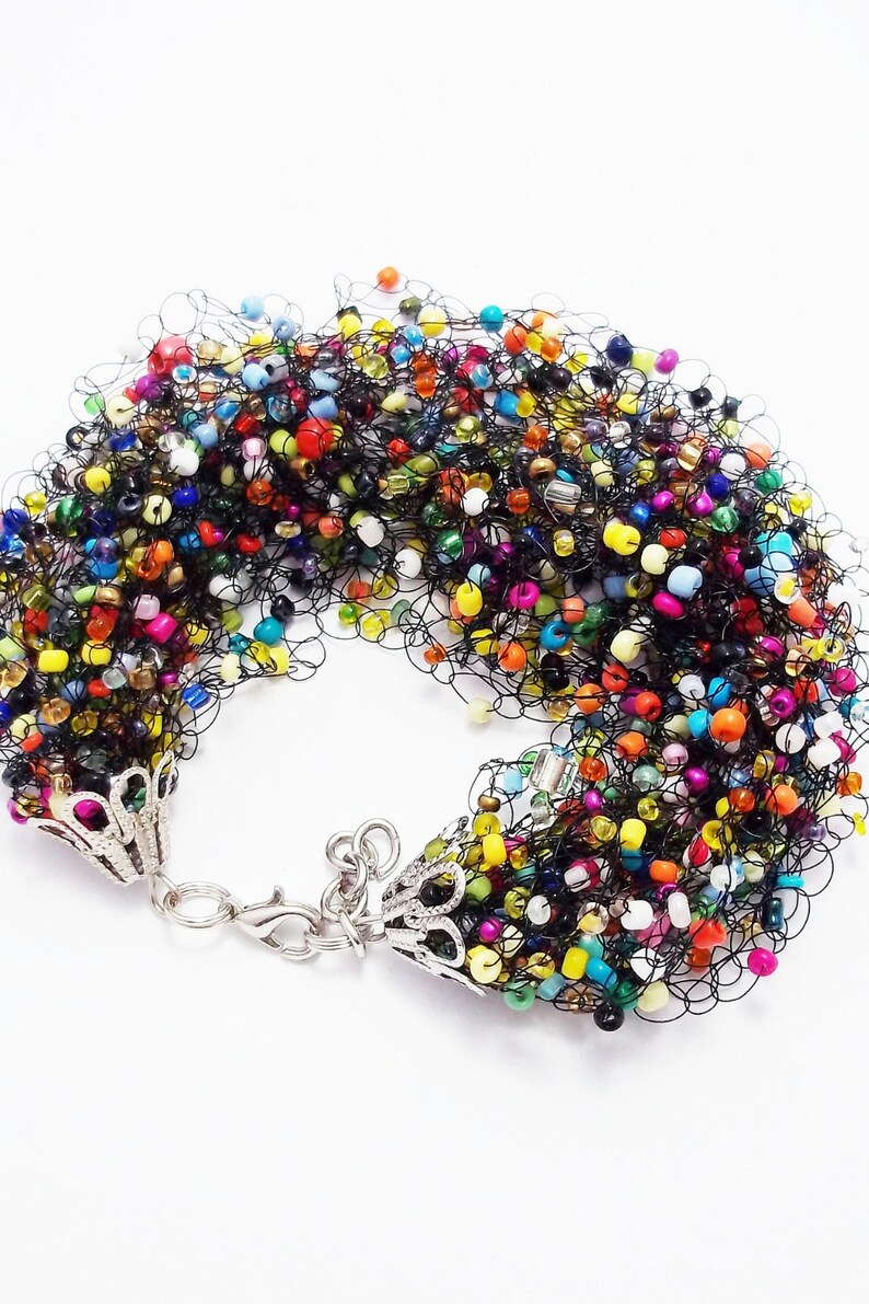 May include: A colorful beaded bracelet with a black crocheted design and silver clasps. The beads are a mix of colors, including red, orange, yellow, green, blue, purple, and white.