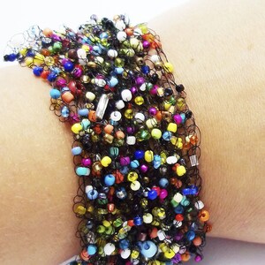 May include: A colorful beaded bracelet with a black crocheted design. The bracelet is made with a variety of small, colorful beads and is strung on a black crocheted cord.