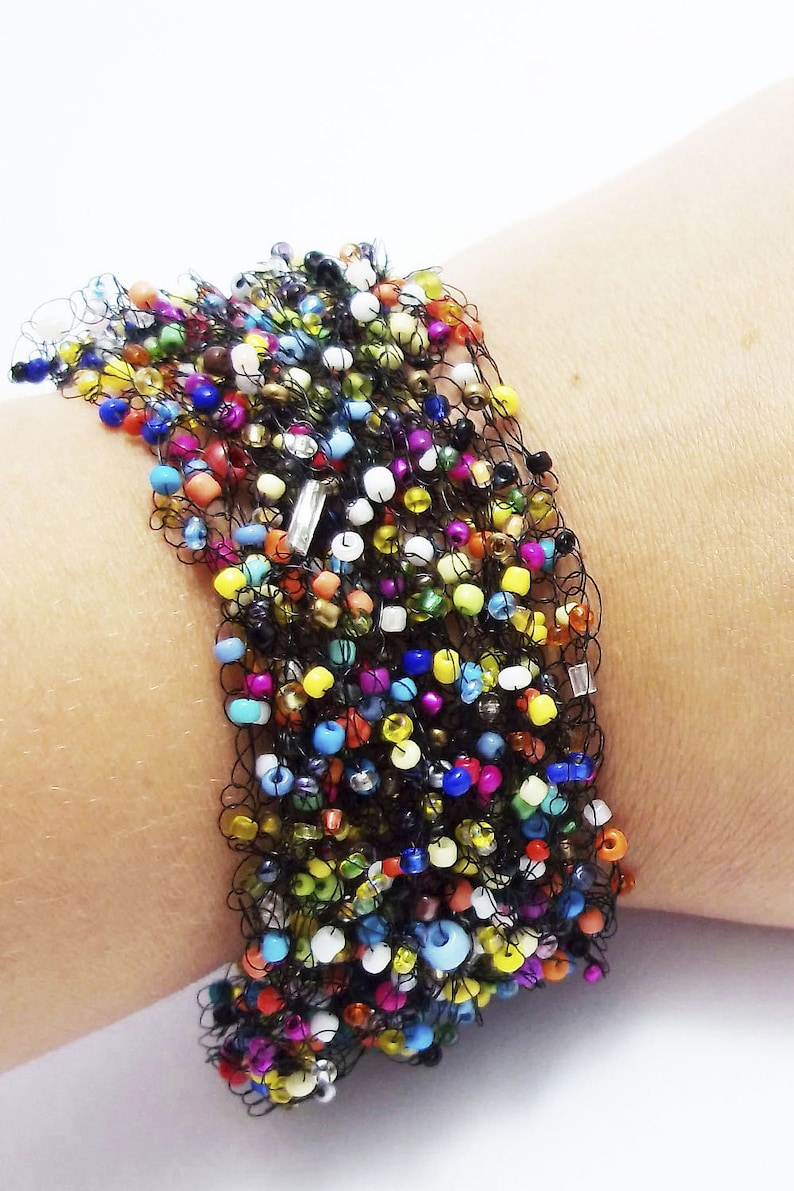 May include: A colorful beaded bracelet with a black crocheted design. The bracelet is made with a variety of small, colorful beads and is strung on a black crocheted cord.
