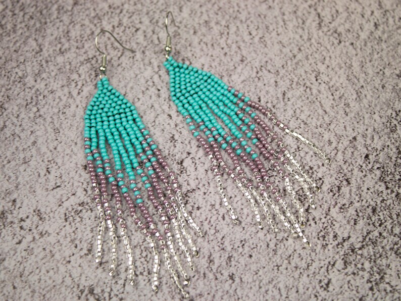 May include: A pair of long, turquoise and purple beaded earrings with silver chain fringe.