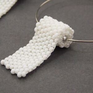 May include: A pair of white beaded earrings, each shaped like a rolled-up piece of paper. The earrings are attached to a silver hoop.