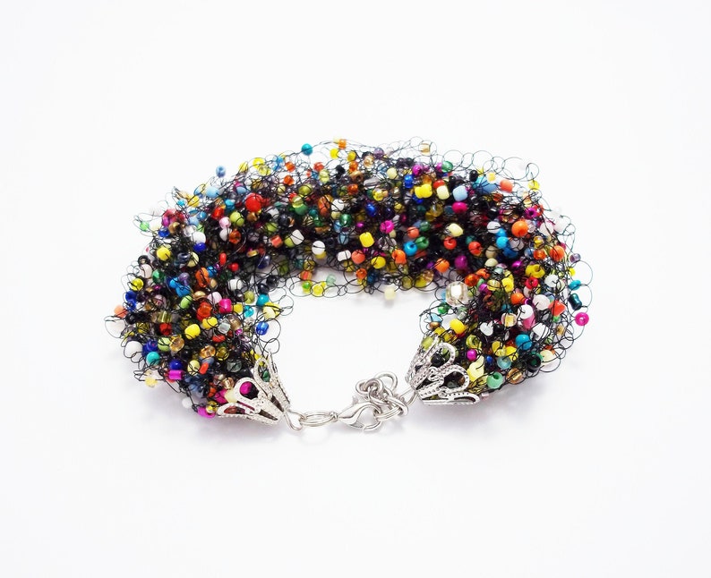 May include: A colorful beaded bracelet with a black crocheted design and silver clasps.