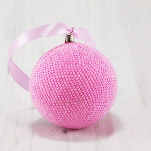 May include: A pink beaded Christmas ornament with a silver loop and a pink ribbon.