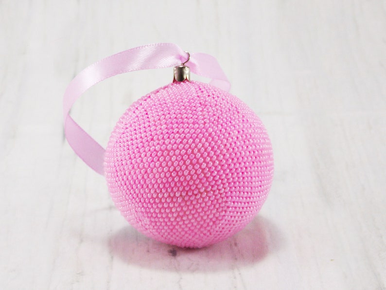 May include: A pink beaded Christmas ornament with a silver loop and a pink ribbon.