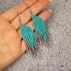 May include: Teal and purple beaded earrings with silver chain fringe. The earrings are long and dangle.