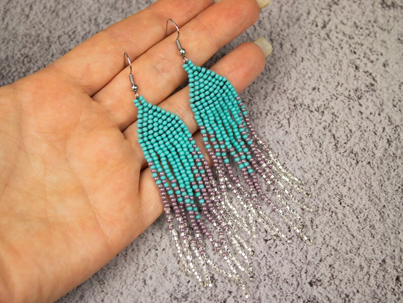 May include: Teal and purple beaded earrings with silver chain fringe. The earrings are long and dangle.