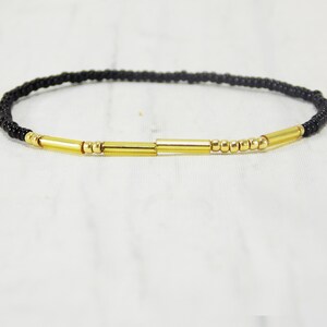 May include: A black beaded bracelet with gold accents. The bracelet has a simple design with small black beads and three gold bars.